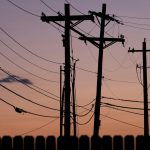 Silhouetted power lines and poles against a vibrant sunset sky, conveying energy and connectivity.