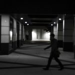 Man walks down a dimly lit, empty hallway.