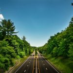 black asphalt road between green trees under blue sky during daytime