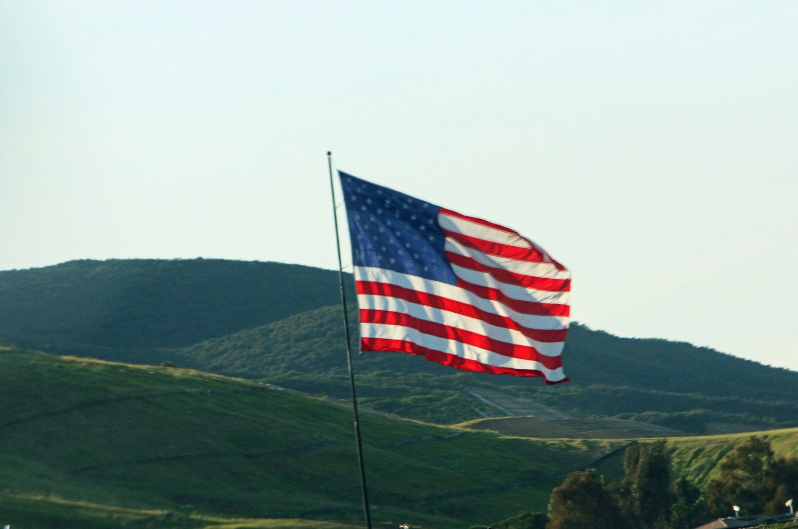 American flag waving on a pole with hills behind