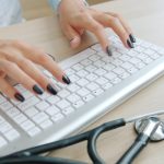 Doctor typing on keyboard with stethoscope nearby