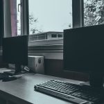 Contemporary computers with black screens placed on desk near window in classroom or office