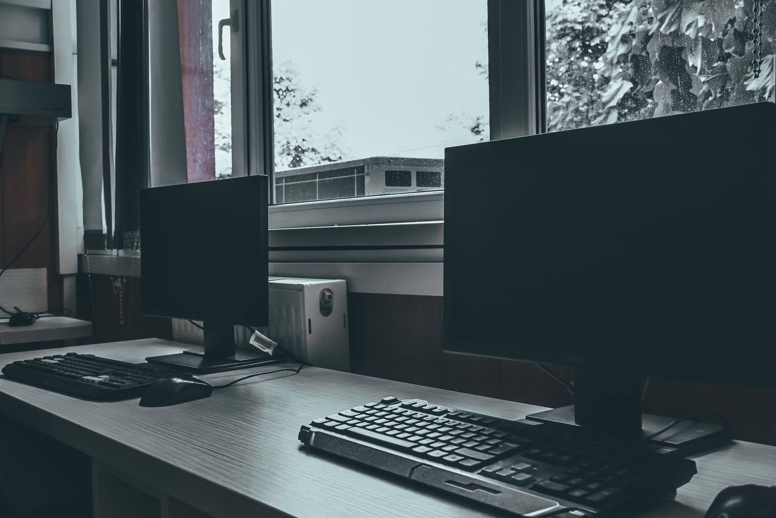 Contemporary computers with black screens placed on desk near window in classroom or office