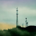 A cell tower on top of a hill next to a forest