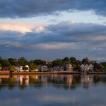 Charming suburban homes reflected in a calm lake under a dramatic twilight sky.